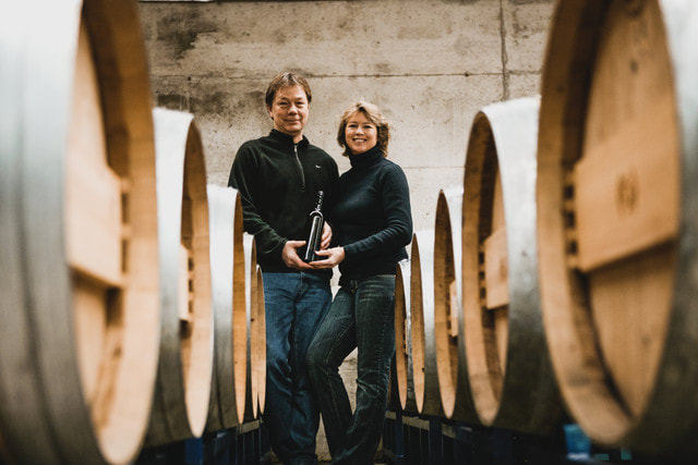 Sue and Gerry owners of Skaha Vineyard in a wine cellar holding one bottle of wine